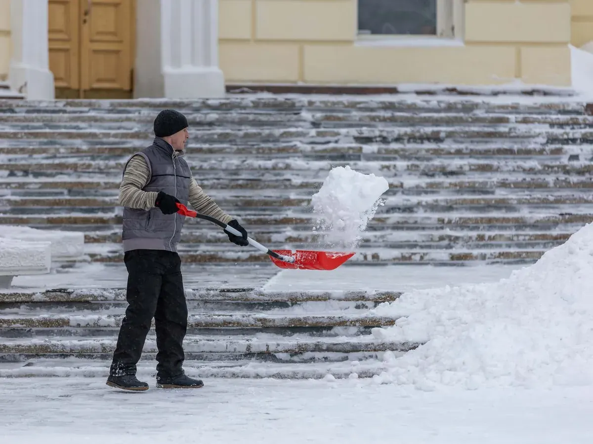 A worker clearing packed snow and ice from a flight of steps