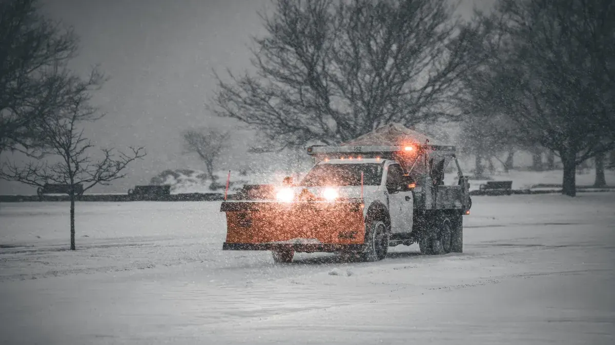 A pickup truck with a plow blade clearing a road in heavy snowfall